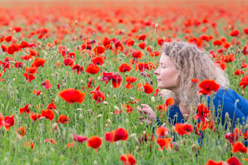 Woman smells red flowers in poppy field