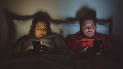 Overweight couple lying in bed and using smartphones late at night - Powered by Adobe