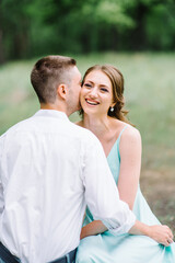 happy guy in a white shirt and a girl in a turquoise dress are walking in the forest park