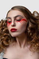 Fototapeta premium Beautiful young woman with clean perfect skin. Portrait of beauty model with bright red make up and long eyelashes. White solid background. Long curly red hair. Close eyes