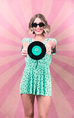 Vintage portrait of a woman, posing, dressed in green, in a pink background, with a vinyl record in...