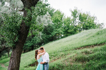 happy guy in a white shirt and a girl in a turquoise dress are walking in the forest park