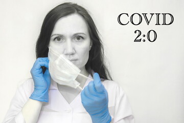 Black and White photo, young female doctor in medical gloves puts a protective mask on her face. The inscription on the Covid 2:0 banner. the concept of the second wave of the covid-19 coronavirus.