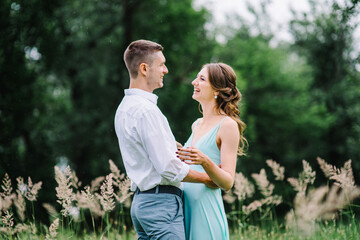 happy guy in a white shirt and a girl in a turquoise dress are walking in the forest park