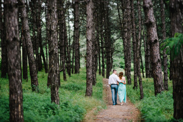 happy guy in a white shirt and a girl in a turquoise dress are walking in the forest park