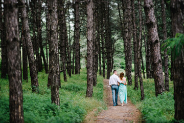 Obraz premium happy guy in a white shirt and a girl in a turquoise dress are walking in the forest park