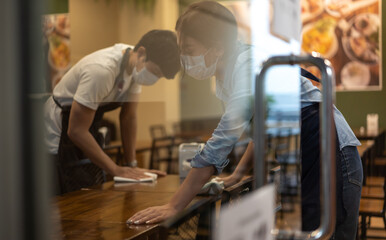 Waiter wearing protective face mask while cleaning tables in restaurant