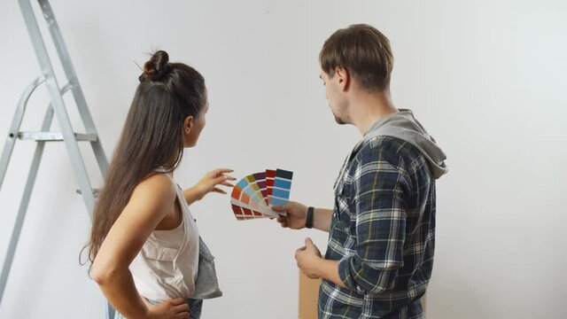 Young happy couple choosing colors for painting wall in new house