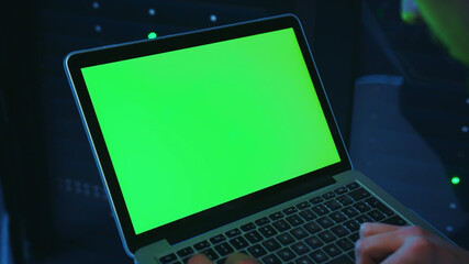 In dark data center, worker holding greenscreen mock-up laptop computer. Close-up IT technician clicking button on notebook activating modern database server cabinet.