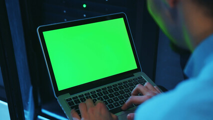 Close-up IT professional male working on neural network greenscreen laptop at server cabinet....