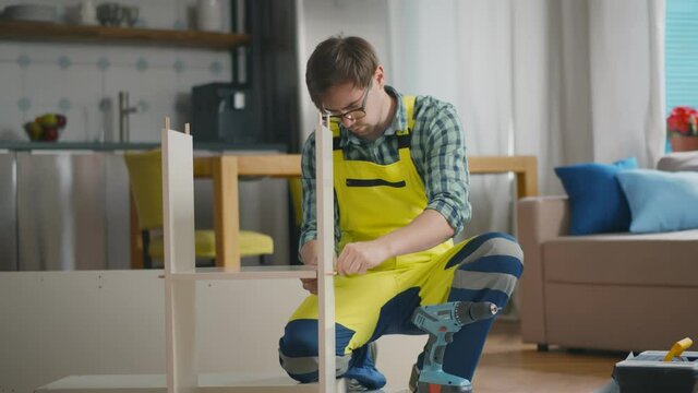 Young repairman in uniform assembling new table at home interior.