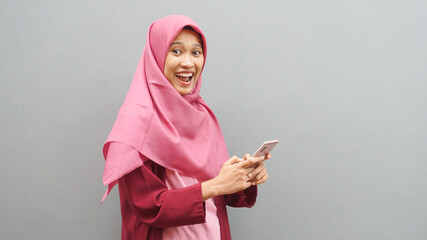 Portrait of young Asian muslim woman wearing hijab get good news on her phone, happy surprised expression