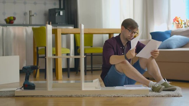 Concentrated young man reading instructions to assemble furniture in kitchen at home.