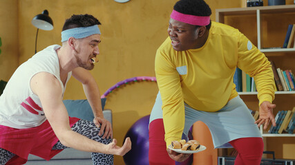 Fototapeta premium Funny two unfit weird retro stylish young men lifting up weight together. Coach helping fat guy working out having fun during home workout. Humor in sports.