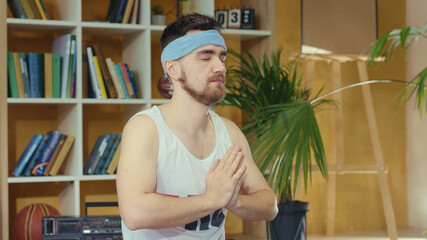 Young caucasian comical man wearing fitness outfit and practicing yoga. Silly jerk retro guy doing meditating asana and spying others opening eyes. Fitness parody concept.