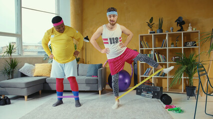 Retro style multi-ethnic men doing home exercising, stretching with elastic bands enjoying workout....