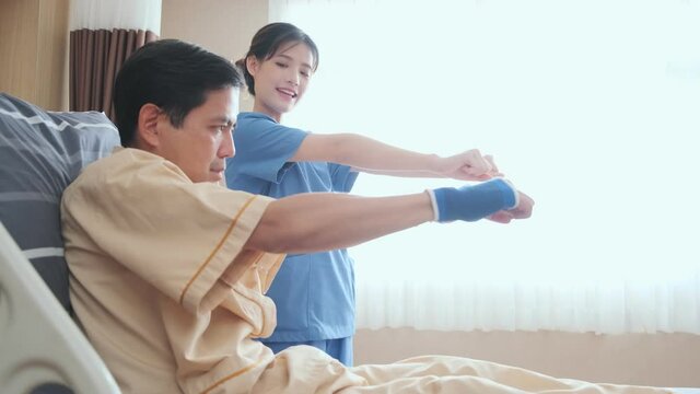 Asian female Physiotherapist working with patient in clinic doing arm stretching exercises with mid adult male patient