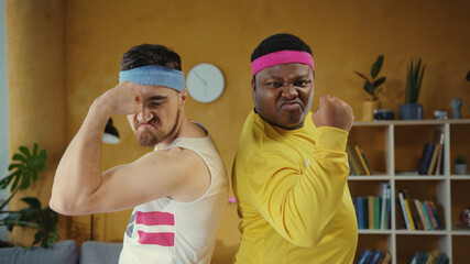 Diverse male couple of unfit weak weird men wearing sportswear, posing back to back looking very self-confident at camera. Sport humor and fun concept.