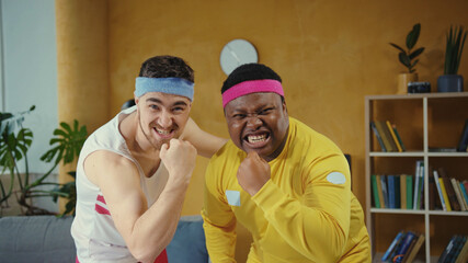 Diverse crazy fitness freaks posing together, boasting of muscles kissing their biceps looking very confident recording funny sports vlog at home.