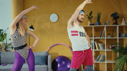 Cheerful young fitness couple stretching their muscles together. Retro style man and woman from 80s doing home exercises warm-up training. Pair workout. Fun concept.