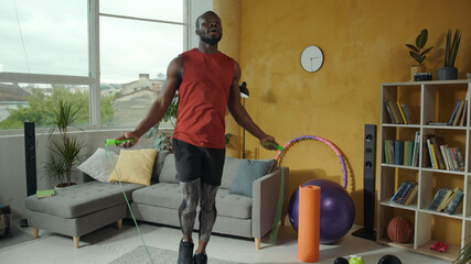 Fototapeta na wymiar Home training. Sporting african american fitness guy jumping with rope exercising indoors. Cardio training. Cross fit. Fitness. Sports and activities.
