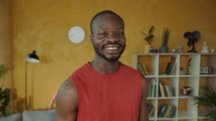 Professional afro-american fitness guy in sportswear standing in living room. Portrait of muscular confident sportsman working out at home.