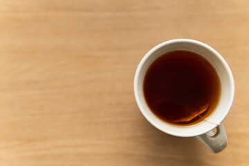 Black tea in white cup placed on wooden table. Focus on tea