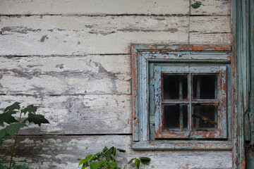 White wall of the very old wooden house with vintage window. Blue wooden window with peeling paint, cracks and scratches.