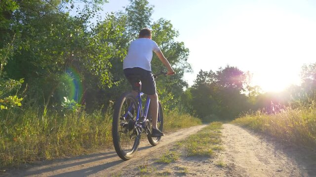 Happy kid riding a bike in a park at sunset. Cycling along the path in the woods in the rays of beautiful sunset. Active rest of the child. Healthy lifestyle, child sports.