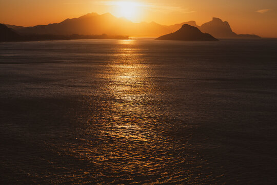 Beautiful yellow sunset over the sea and behind mountains reflecting on the sea. Sunrise over the ocean with golden sun rising from behind the mountain.
