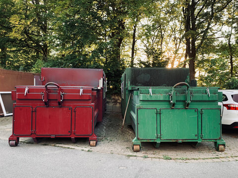 On An Industrial Site A Green Waste Compactor And A Red Waste Compactor Stand Side By Side