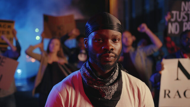 Serious African American Activist With Effective Placard Stands In Front Of Shouting Crowd Protesting For Justice, Freedom And Peace. Black Lives Matter. Street Riot.