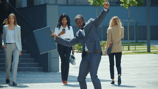Happy energetic black businessman dancing on streetin sunny weather. Successful entrepreneur celebrating hsi business triump. Corporate people. Office crowd.