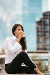 Businesswoman having a break from work sitting and relaxing with a coffee to go in front of the glass office.