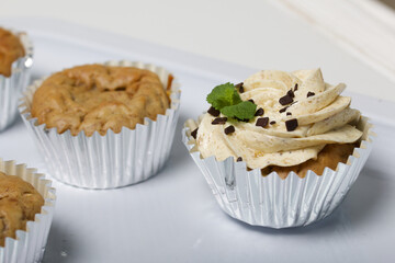 Banana cupcake. With butter cream and banana jam. Decorated with mint leaves and chocolate sprinkles. Next to them are cupcakes without cream