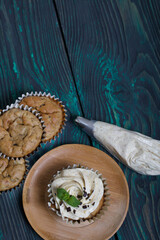 Banana cupcake. With butter cream and banana jam. Decorated with mint leaves and chocolate sprinkles. Next to them are cupcakes without cream and a pastry bag with cream.
