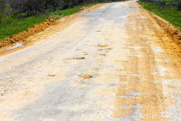 A road damaged by rain and snow, that is in need of maintenance. Broken asphalt pavement resulting in a pothole, dangerous to vehicles.