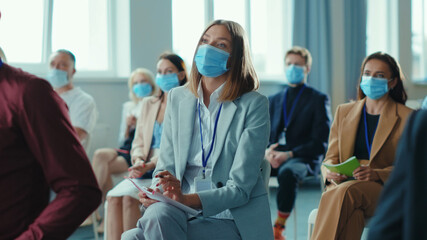 Fototapeta na wymiar Caucasian young businesswoman participates in trading education forum for corporate workers in large conference room. Business seminar. Face masks. Quarantine. Workspace.