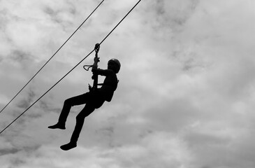 Closeup of a man gliding on extreme trolley zip-line in adventure park. Silhouette image. 