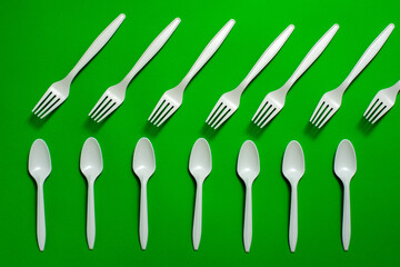 organic disposable cornstarch forks and spoons laid out on a green background. isolate. eco friendly. modern replacement of plastic dishes with biodegradable materials.