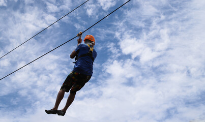 Closeup of a man gliding on extreme trolley zip-line in adventure park with cloudy blue sky background. 