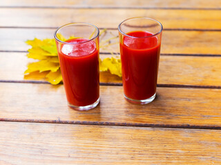 Tomato juice in a glass cup and yellow autumn leaves on a wooden table. Selective focus.
