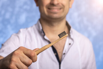 bamboo toothbrush close-up in male hands. eco friendly concept. blue background. daily oral hygiene.