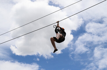 Closeup of a woman gliding on extreme trolley zip-line in adventure park with cloudy blue sky background. 