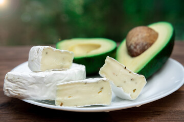 sliced white brie or camembert cheese and half an avocado on a white plate. healthy diet. an option for a beautiful presentation of lunch.