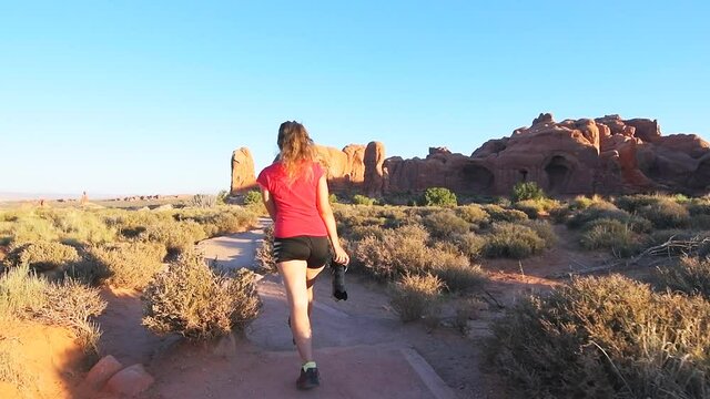 Slow motion of walking behind young woman back on hiking trail to Double arch in Arches National Park in Utah in summer, taking photo picture photographing with professional telephoto lens camera