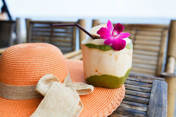 Coconut juice drink with a flower, summer hat on a table. Holiday in a tropical country.