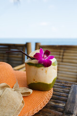 Coconut juice drink with a flower, summer hat on a table. Holiday in a tropical country.