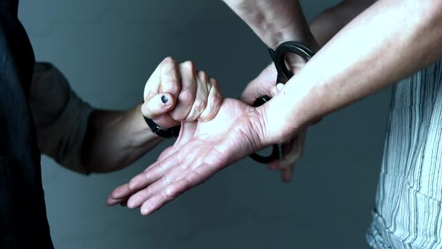 Professional handcuffing of a criminal behind his back close up. Theme of law enforcement, crime and justice. Man is arrest by close his hands cuffs. Hands of police officer and criminal close-up.