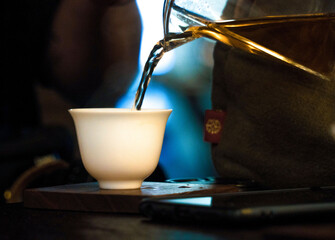 Traditional Chinese Tea Ceremony. Black or Red Tea pouring from a glass seethrough Chahai into White pial cup on dark wooden Table background